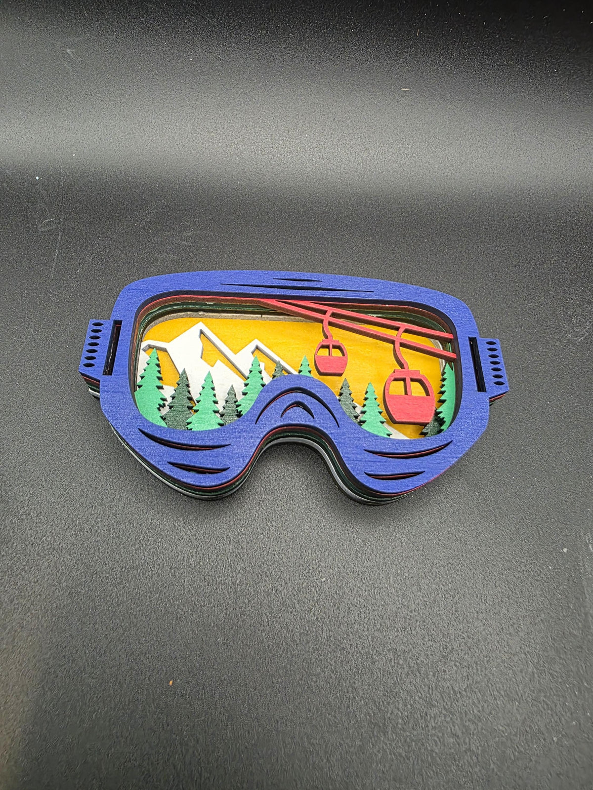 Blue-framed 3D wood ski lift ornament with red gondolas over a yellow sky and pine trees