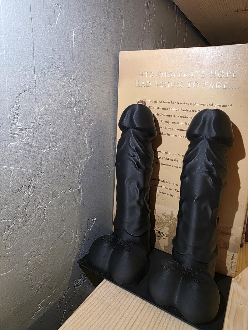 Black Balls Deep penis bookends holding a book, side view