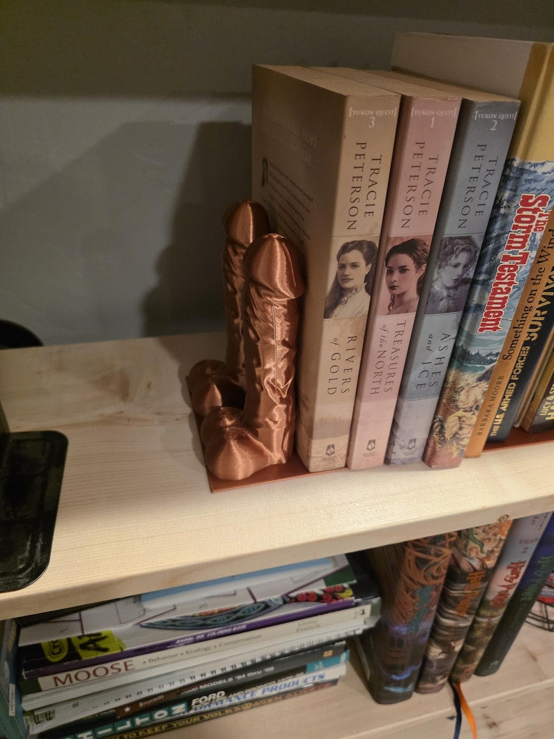 Copper Balls Deep penis bookend holding paperbacks on a shelf