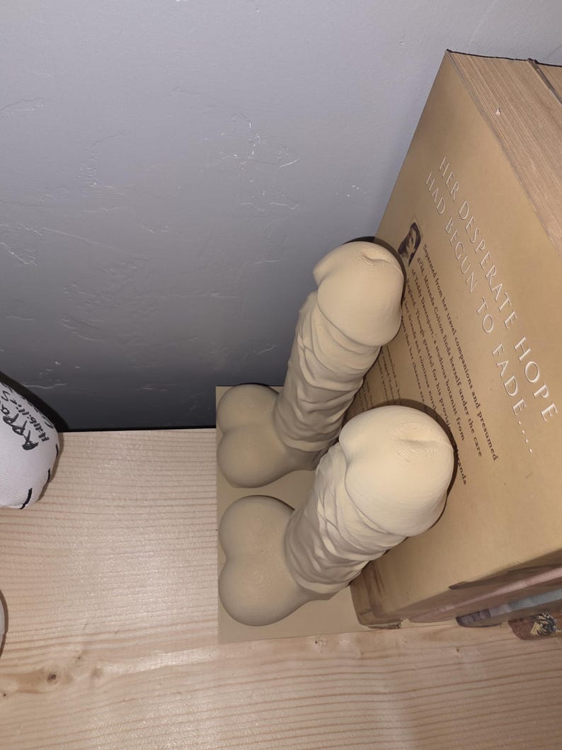 Beige Balls Deep penis bookends, close side view against a book