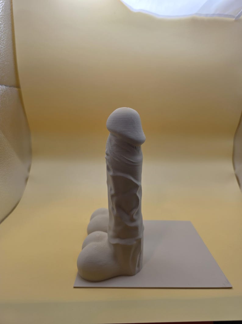 Single gray-brown Balls Deep penis bookend on a base plate, side view