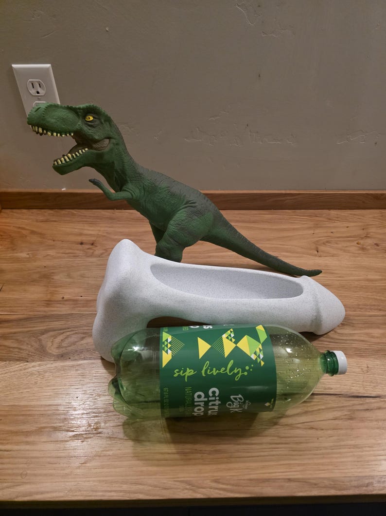 Oversized penis planter shown with dinosaur and soda bottle