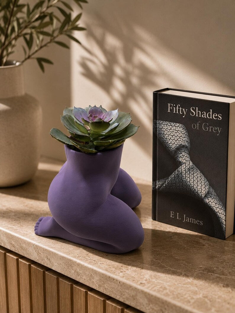 Purple Mrs. Gray kneeling body planter with a succulent beside a book