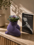Purple Mrs. Gray kneeling body planter with a succulent beside a book